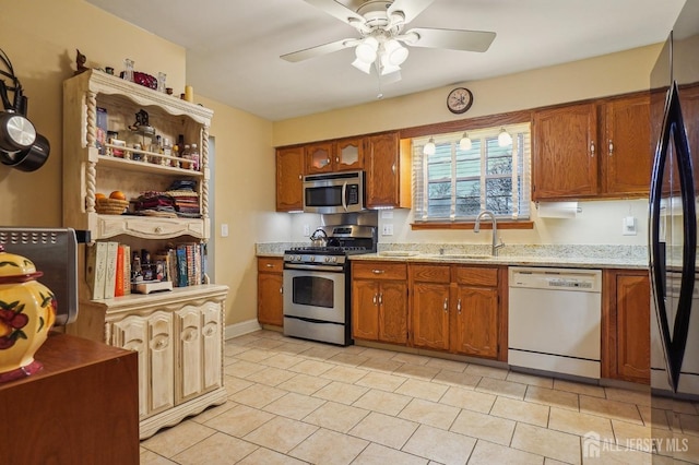 kitchen with light stone counters, stainless steel appliances, light tile patterned floors, ceiling fan, and sink