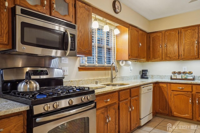 kitchen with sink, light tile patterned flooring, light stone counters, and appliances with stainless steel finishes