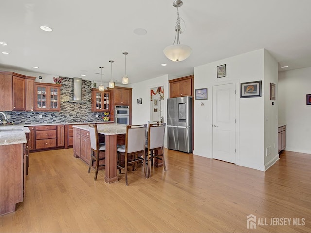 6 Condor Ct, South Brunswick, NJ 08852 - kitchen featuring appliances with stainless steel finishes, wall chimney exhaust hood, brown cabinetry, decorative backsplash, and a kitchen island
