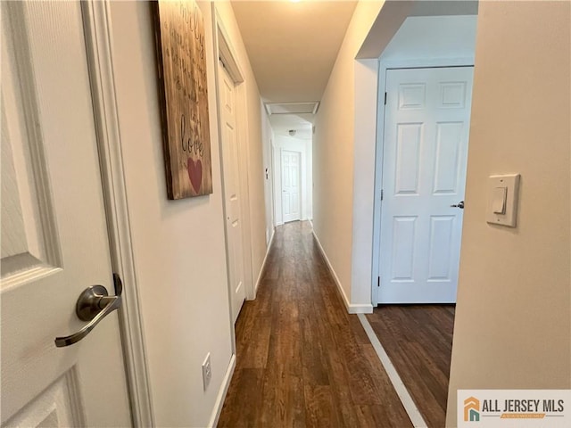 hallway featuring attic access, dark wood-style floors, and baseboards