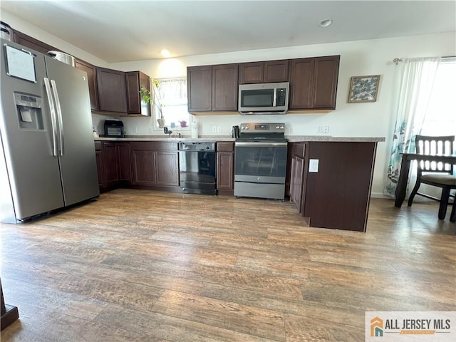 kitchen with dark brown cabinets, appliances with stainless steel finishes, light wood-style flooring, and light countertops