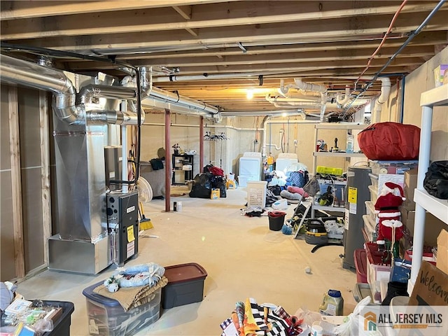 unfinished below grade area featuring water heater, heating unit, and washing machine and dryer