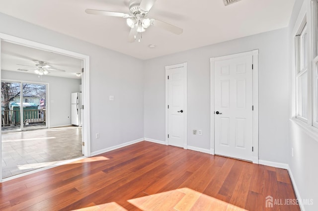 unfurnished bedroom featuring freestanding refrigerator, wood finished floors, baseboards, and a ceiling fan
