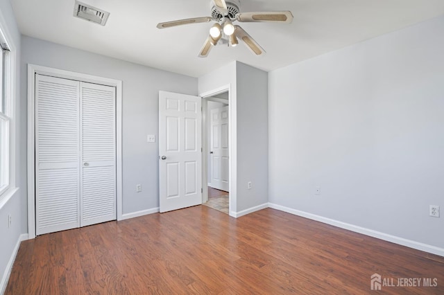 unfurnished bedroom featuring baseboards, wood finished floors, a closet, and a ceiling fan