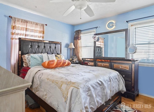 bedroom with wood finished floors, multiple windows, a ceiling fan, and baseboards