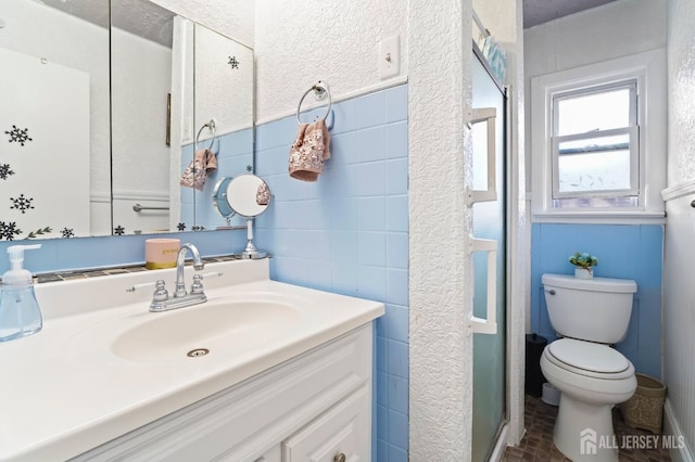 bathroom with tile walls, vanity, toilet, and a shower stall