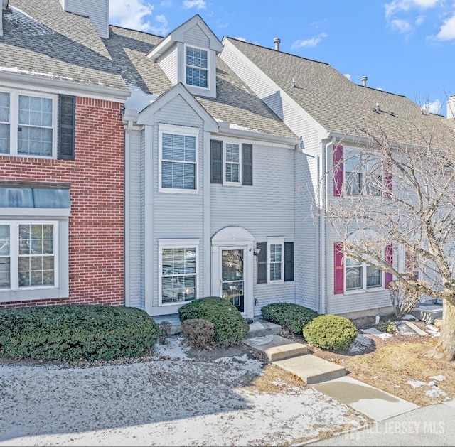 townhome / multi-family property featuring roof with shingles, brick siding, and a chimney