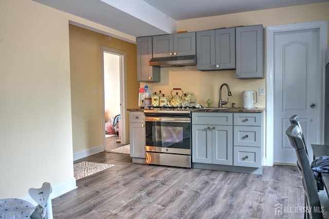 kitchen with gas range, a sink, under cabinet range hood, light wood-type flooring, and gray cabinets