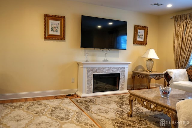 living area with baseboards, wood finished floors, a stone fireplace, and recessed lighting