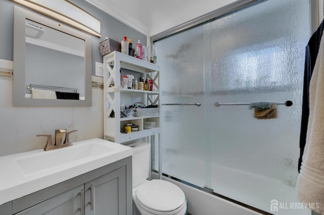 full bathroom featuring decorative backsplash, ornamental molding, vanity, shower / bath combination with glass door, and toilet