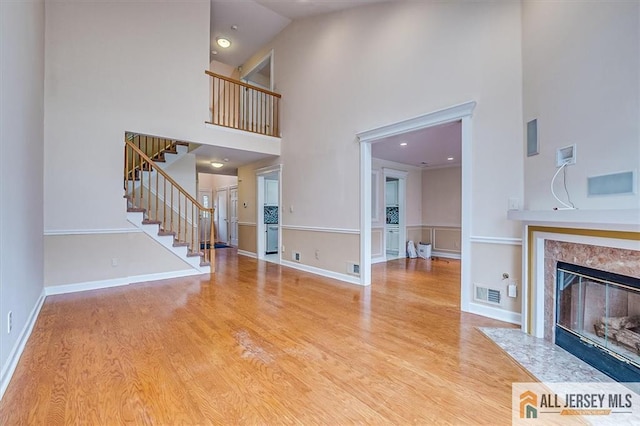 unfurnished living room with a high ceiling, stairs, wood finished floors, a fireplace, and recessed lighting