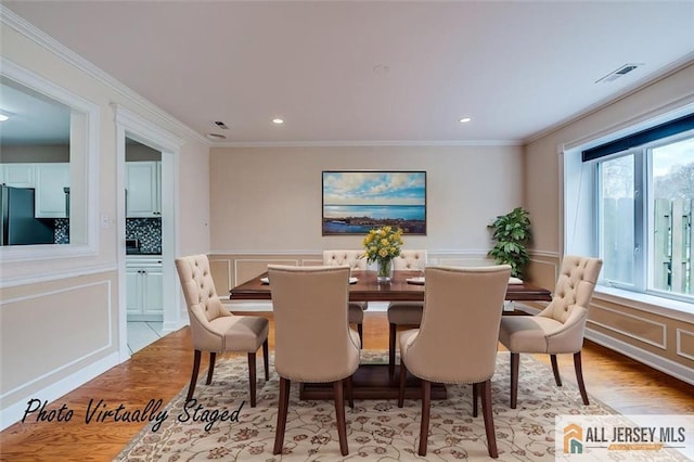 dining space with light wood-style floors, recessed lighting, a decorative wall, and crown molding