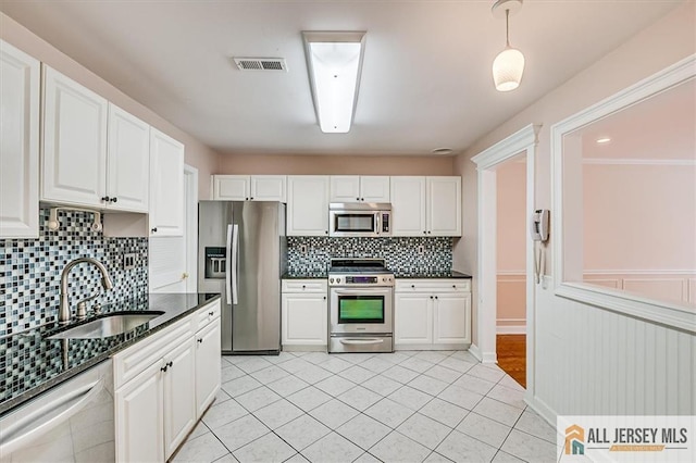 kitchen with appliances with stainless steel finishes, a sink, backsplash, white cabinets, and light tile patterned flooring