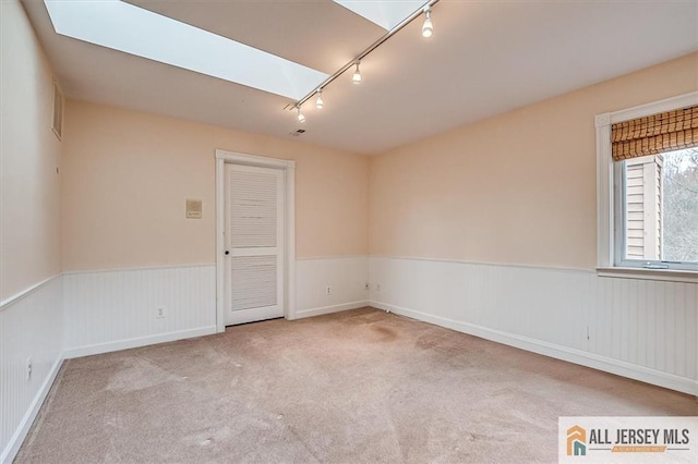 carpeted spare room featuring rail lighting, a wainscoted wall, and a skylight