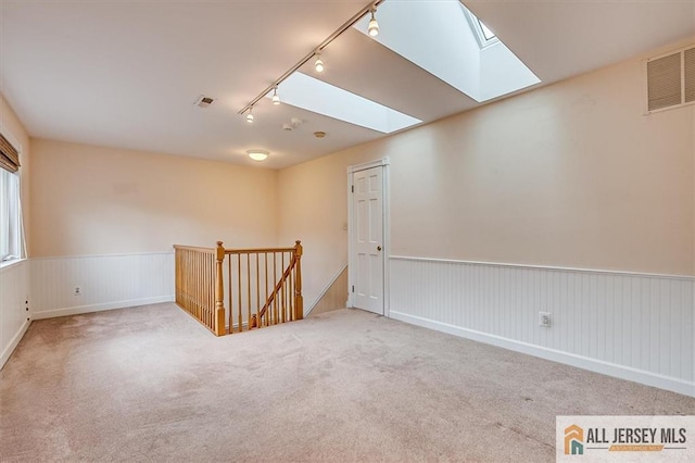 carpeted empty room featuring a skylight, track lighting, and a wainscoted wall