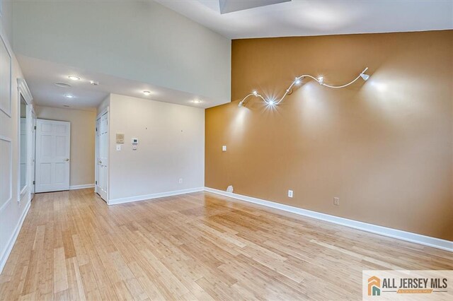 spare room with light wood-type flooring, baseboards, and high vaulted ceiling