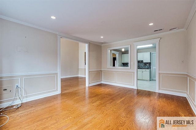 empty room with a decorative wall, ornamental molding, light wood finished floors, and recessed lighting