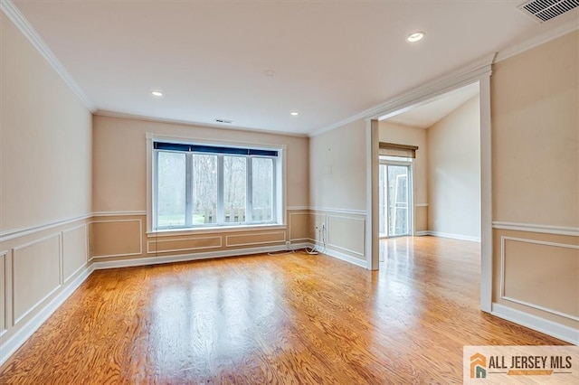 empty room with ornamental molding, light wood-type flooring, a wainscoted wall, a decorative wall, and recessed lighting