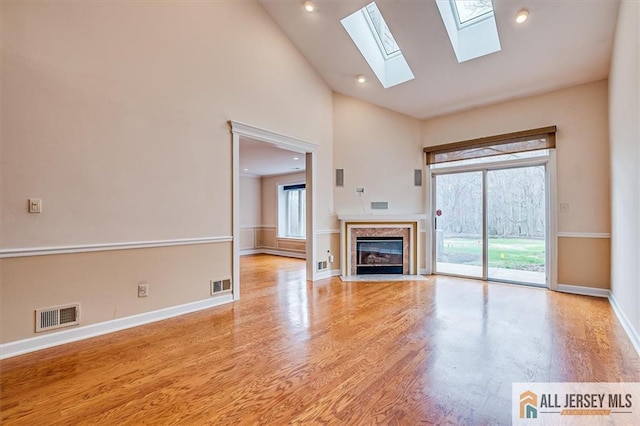 unfurnished living room with a skylight, wood finished floors, baseboards, a premium fireplace, and high vaulted ceiling