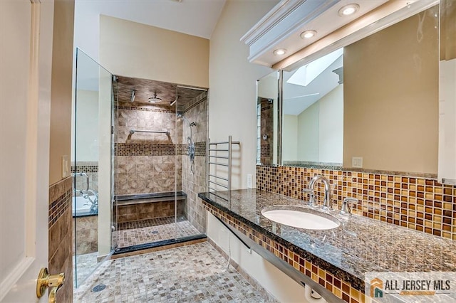 bathroom with a shower stall, a skylight, vanity, backsplash, and tile patterned flooring