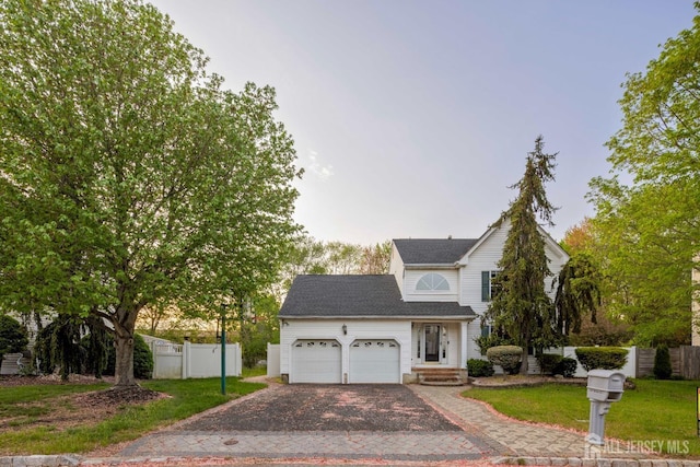 traditional-style house with a garage, a front lawn, fence, roof with shingles, and driveway