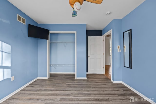 unfurnished bedroom featuring baseboards, a closet, wood finished floors, and visible vents