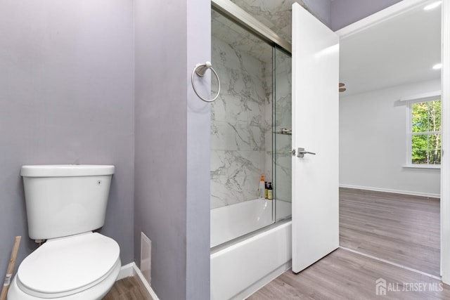 bathroom featuring baseboards, combined bath / shower with glass door, wood finished floors, and toilet