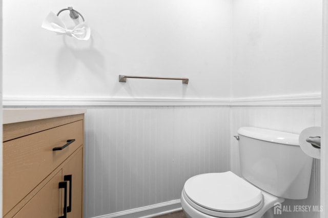 half bathroom with vanity, a wainscoted wall, and toilet