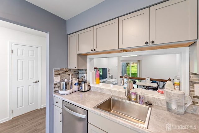 kitchen with stainless steel dishwasher, tasteful backsplash, a sink, and light countertops