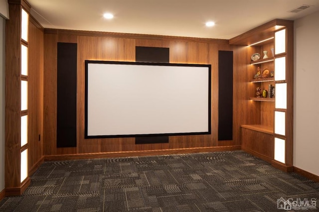 carpeted home theater room with built in shelves and wooden walls