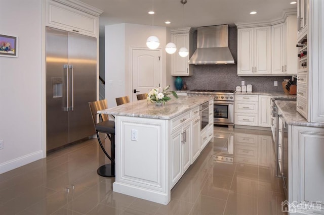 kitchen featuring decorative light fixtures, built in appliances, wall chimney exhaust hood, a center island, and tile patterned flooring