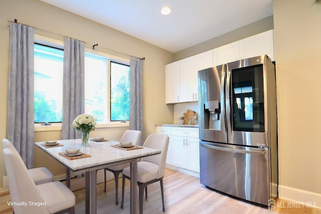 kitchen with white cabinets, stainless steel fridge, light wood-type flooring, and light stone counters