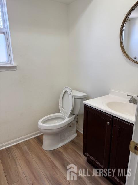 half bath featuring vanity, wood finished floors, toilet, and baseboards