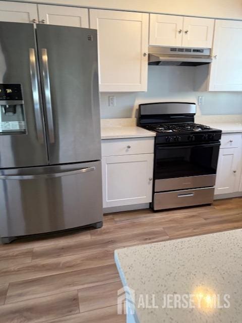 kitchen with under cabinet range hood, white cabinets, light countertops, gas range oven, and stainless steel fridge