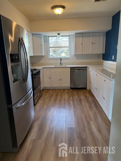 kitchen with dark wood finished floors, stainless steel appliances, light countertops, white cabinetry, and a sink