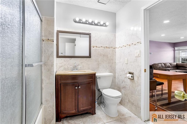 full bathroom featuring toilet, a textured ceiling, tile walls, enclosed tub / shower combo, and vanity