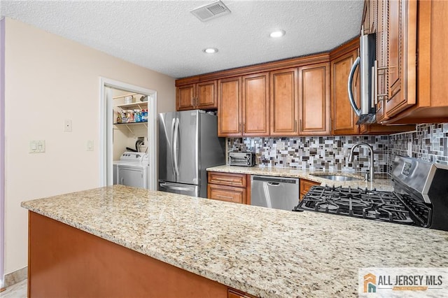 kitchen featuring stainless steel appliances, sink, washing machine and clothes dryer, a textured ceiling, and light stone counters