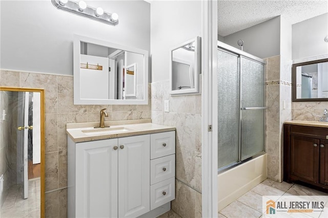 bathroom featuring tile walls, a textured ceiling, enclosed tub / shower combo, and vanity