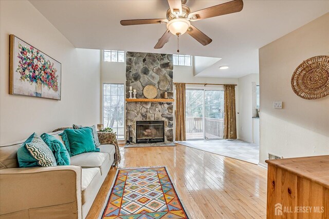 living room featuring ceiling fan, a stone fireplace, and light hardwood / wood-style floors