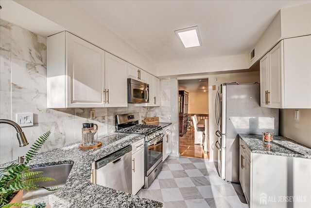 kitchen with decorative backsplash, sink, white cabinetry, light stone countertops, and appliances with stainless steel finishes