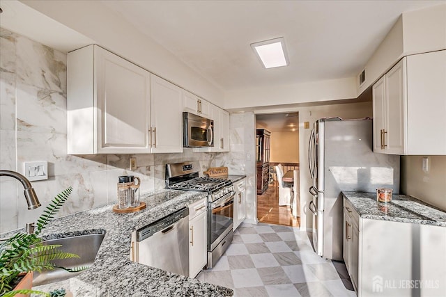 kitchen featuring sink, white cabinetry, tasteful backsplash, stainless steel appliances, and light stone countertops