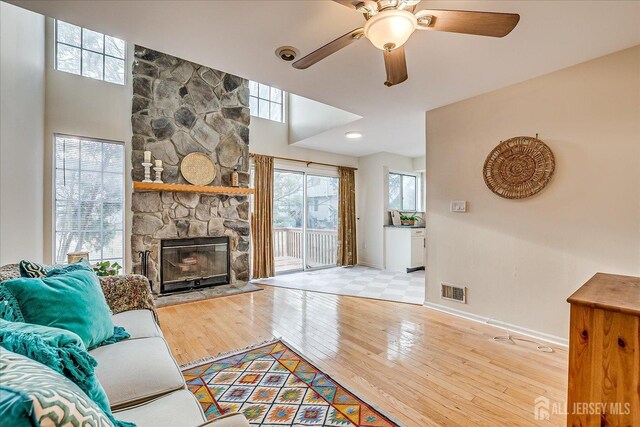 living room with ceiling fan, a healthy amount of sunlight, a stone fireplace, and light hardwood / wood-style floors