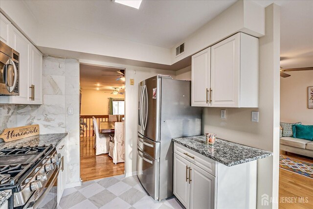 kitchen featuring tasteful backsplash, ceiling fan, white cabinetry, stainless steel appliances, and dark stone counters