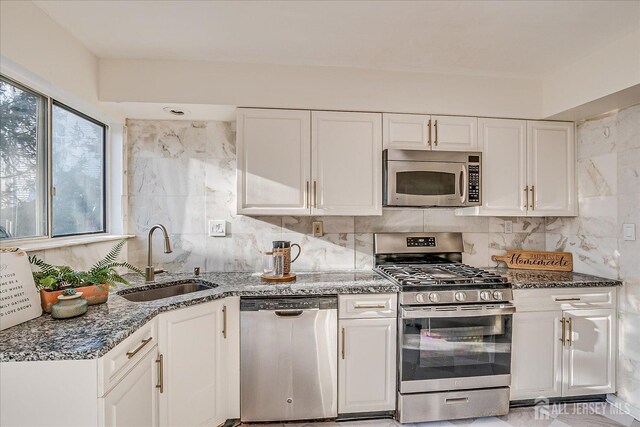 kitchen featuring backsplash, sink, white cabinetry, appliances with stainless steel finishes, and dark stone counters