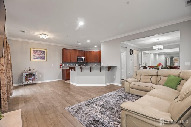 living room featuring an inviting chandelier, crown molding, and light wood-type flooring