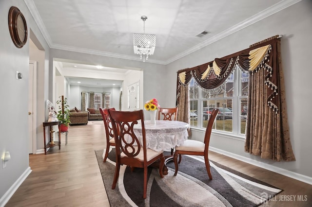 dining space with hardwood / wood-style flooring, crown molding, and a notable chandelier