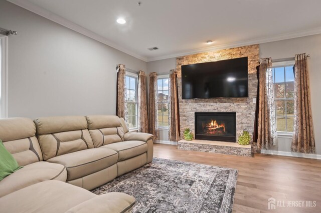 living room featuring ornamental molding, a stone fireplace, a wealth of natural light, and light hardwood / wood-style floors