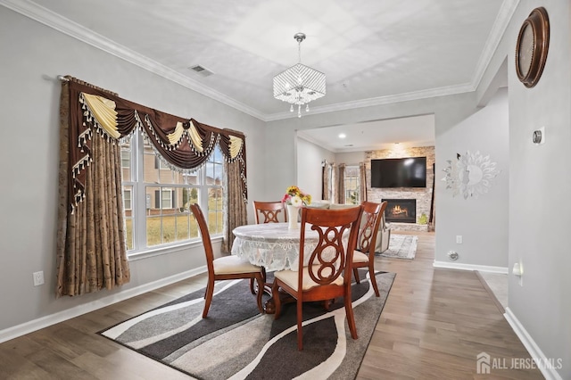 dining space featuring wood-type flooring, ornamental molding, a fireplace, and a chandelier