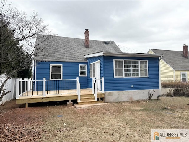 rear view of property featuring a shingled roof, a chimney, and a deck