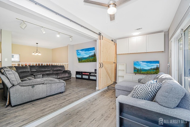 living room featuring a notable chandelier, a barn door, rail lighting, light wood-style flooring, and visible vents